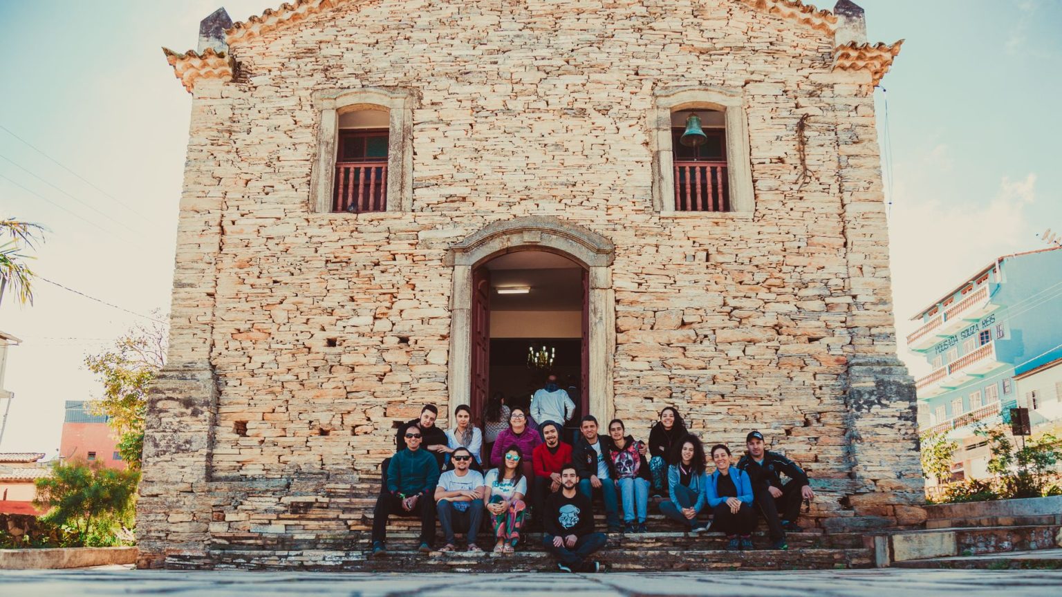 Grupo de pessoas reunido nos degraus diante de uma igreja histórica de pedra.