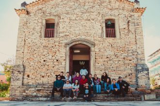 Grupo de pessoas reunido nos degraus diante de uma igreja histórica de pedra.