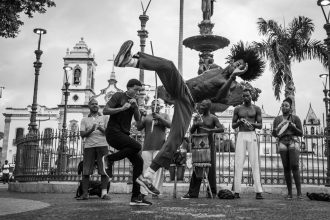 Apresentação de capoeira em uma rua do centro histórico de Salvador, com dançarinos em movimento diante de edifícios coloniais.