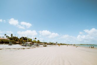 Praia de Flecheiras, no Ceará, em dia ensolarado, com barcos e coqueiros à margem do mar.