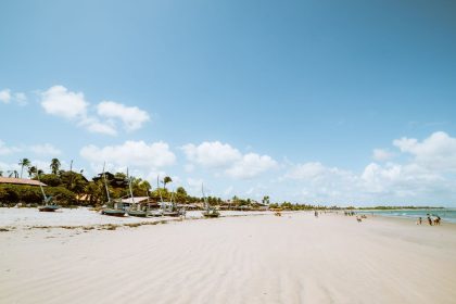 Praia de Flecheiras, no Ceará, em dia ensolarado, com barcos e coqueiros à margem do mar.
