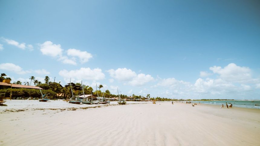 Praia de Flecheiras, no Ceará, em dia ensolarado, com barcos e coqueiros à margem do mar.