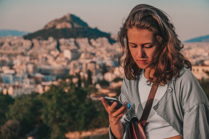 Mulher usa o smartphone diante de uma paisagem urbana de Atenas, na Grécia.