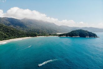 Vista aérea da costa verdejante da Ilha Grande, com águas azul-turquesa e trechos de Mata Atlântica.