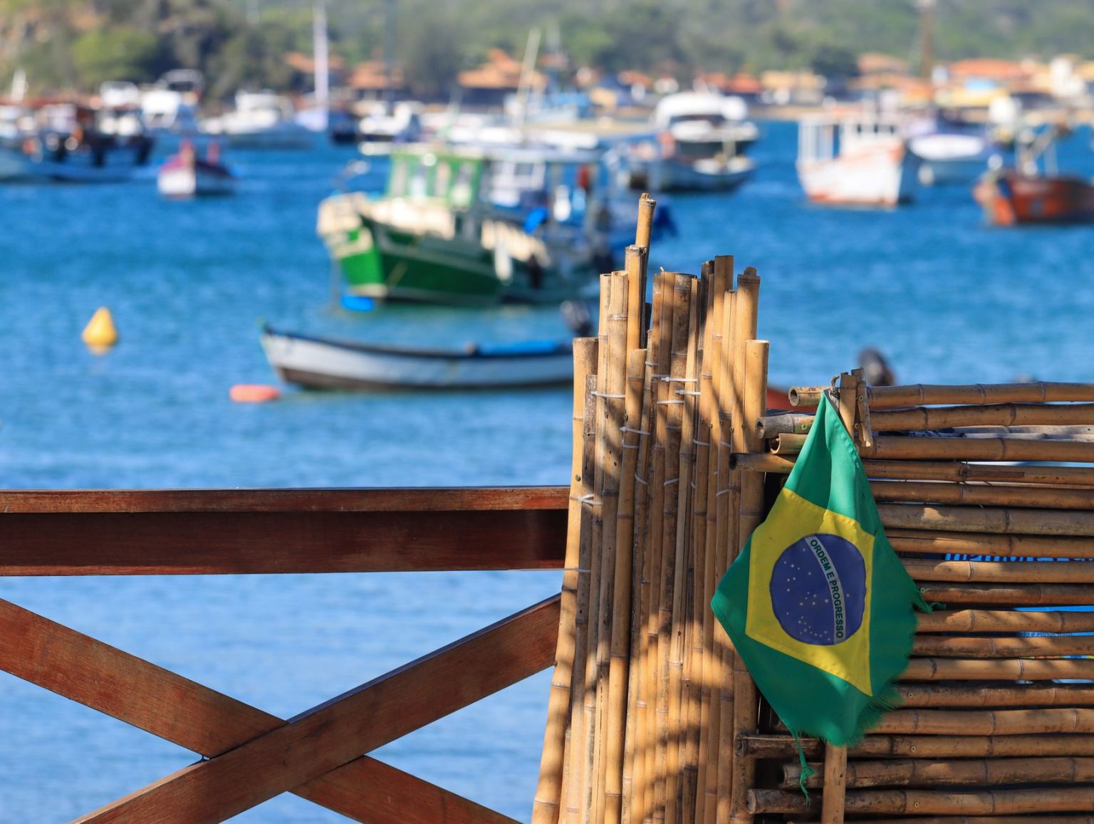 Bandeira do Brasil diante de barcos ancorados em uma baía litorânea.