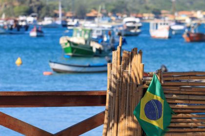 Bandeira do Brasil diante de barcos ancorados em uma baía litorânea.