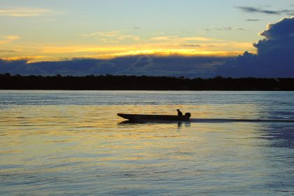 Rio de Porto Velho ao entardecer, com uma embarcação sobre a água e o horizonte ao fundo