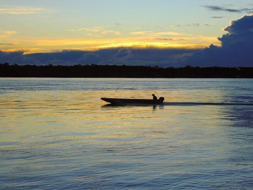 Rio de Porto Velho ao entardecer, com uma embarcação sobre a água e o horizonte ao fundo